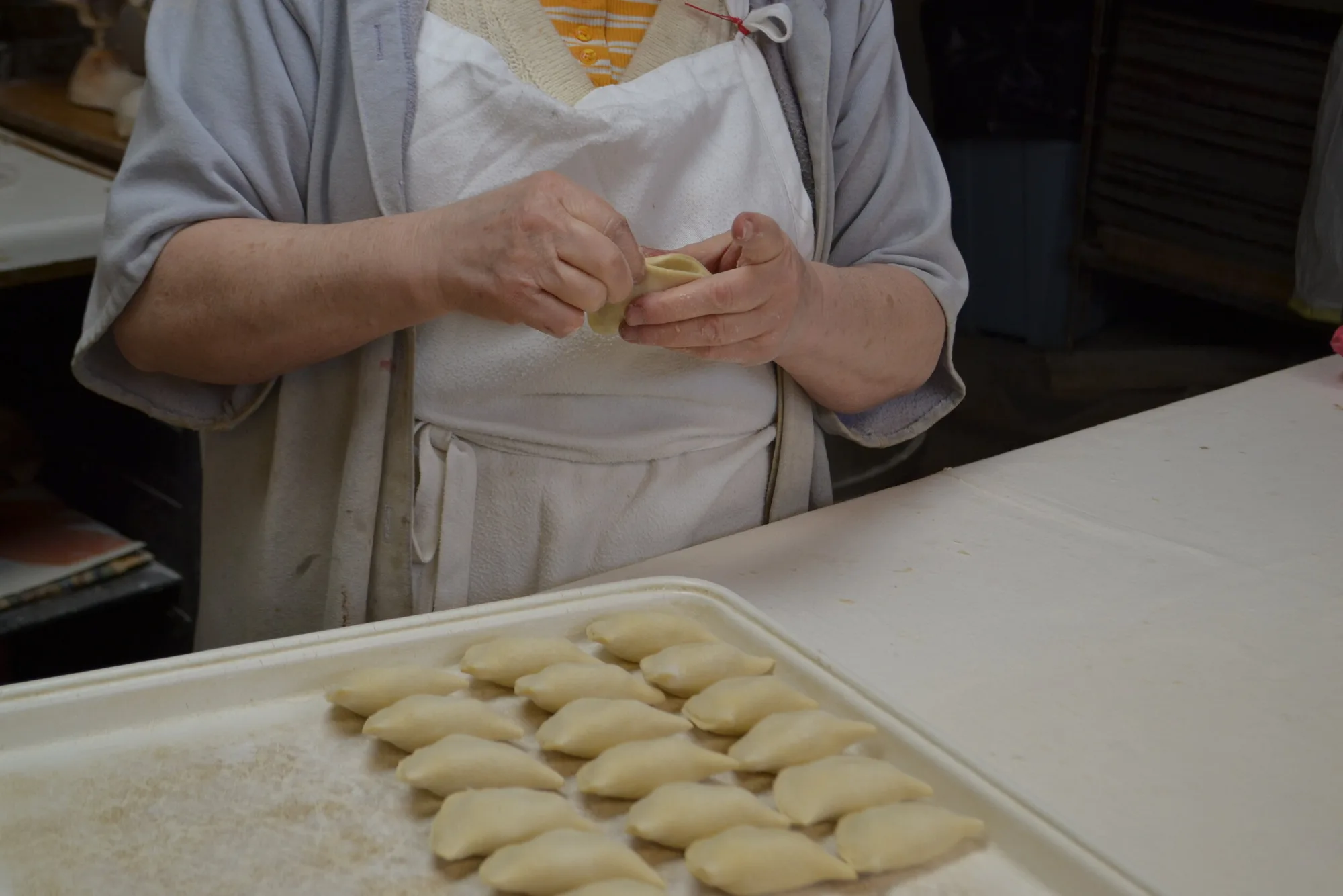 Baker shaping pierogi by hand on a sheet tray