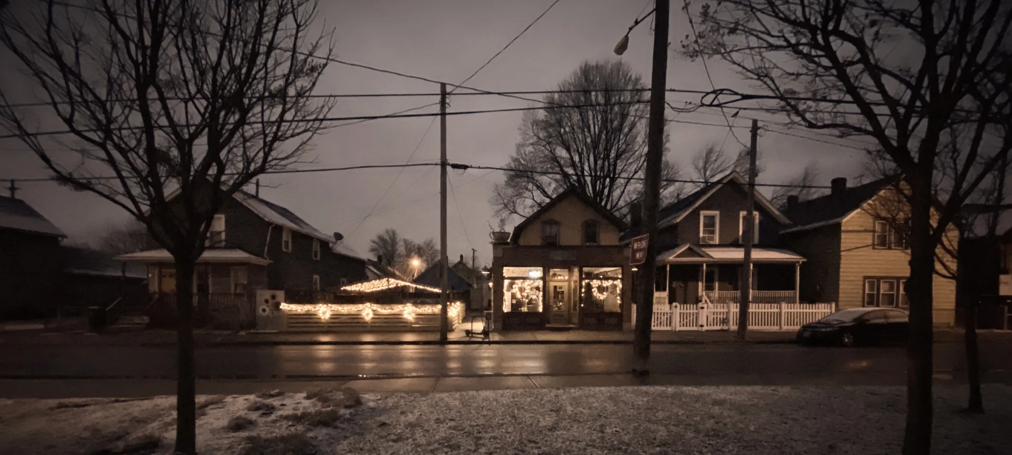 Neighborhood street corner at dusk with lit storefront windows